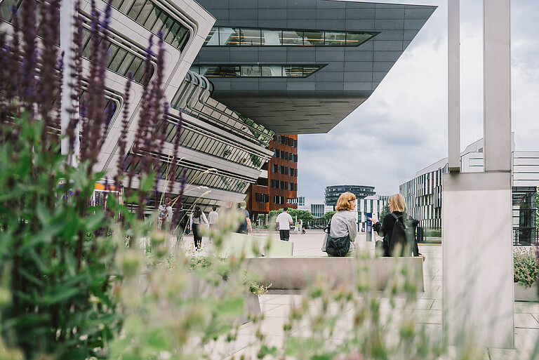 Unternehmensexpansion nach Wien: Beratungen und Förderungen für Unternehmen und Startups. Zwei Frauen sitzen auf einer Bank auf einem Platz der Wirtschaftsuniversität Wien.