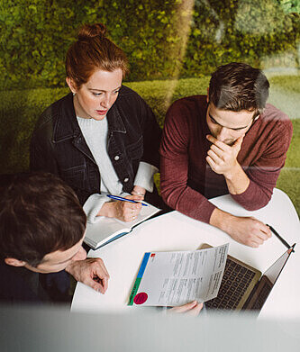 Eine Frau und zwei Männer stzen gemeinsam an einem Tisch. Sie diskutieren und beraten sich