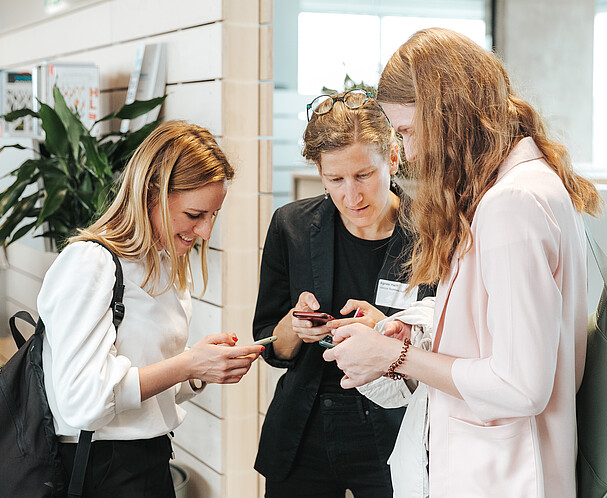 Drei Frauen stehen zusammen und tauschen Kontakte aus. Sie haben dazu Handys in der Hand
