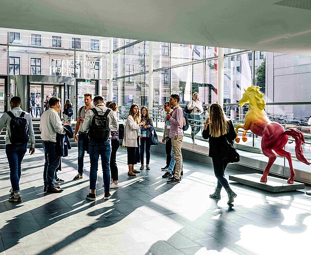 A large group of people in the hallway of a glass-walled building.