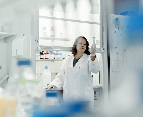 Laborplätze für Startups in Wien Eine Frau mit Laborkittel und Gummihandschuhen hält ein durchsichtige Flasche in der Hand und betrachtet den Inhalt