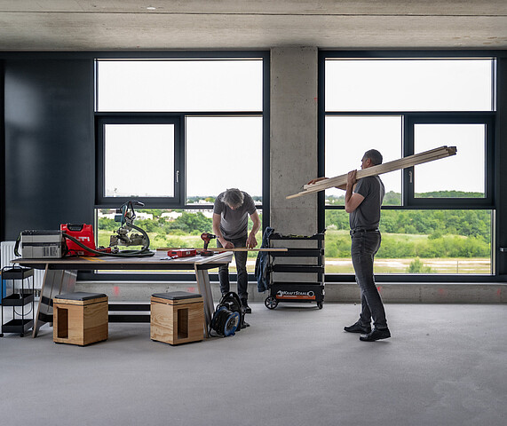 Zwei Männer arbeiten in einem Raum an einem Holzwerkstück.