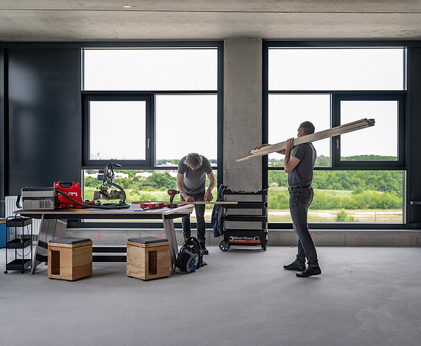 Zwei Männer arbeiten in einem Raum an einem Holzwerkstück.