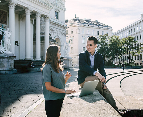 Eine Frau links und ein Mann mit Laptop am Karlsplatz