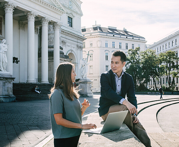 Eine Frau links und ein Mann mit Laptop am Karlsplatz