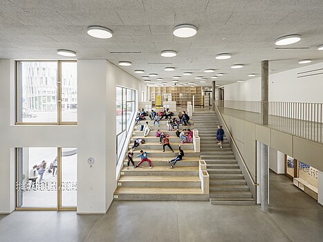 Blick in die Aula einer Volksschule, Kinder sitzen auf einer Treppe