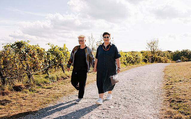 Bistra und Christa: Zwei Frauen gehen Hand in Hand auf einem Schotterweg in den Weinbergen spazieren