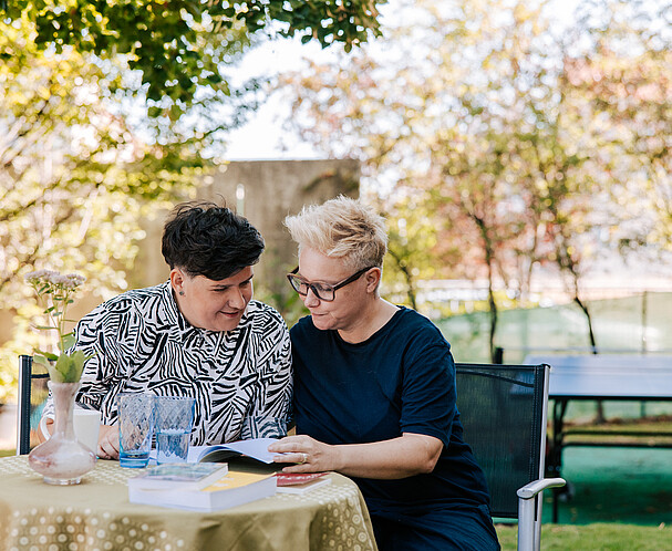 Bistra and Christina Two women sitting at a table, reading a book together.