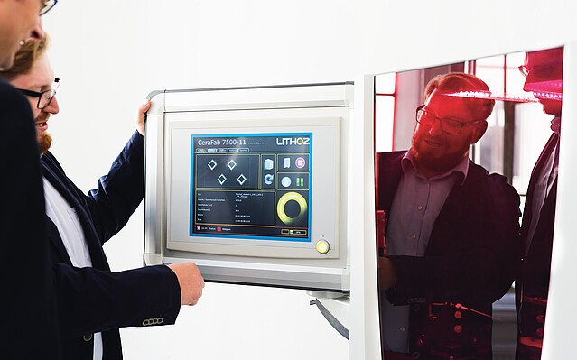 Lithoz_3DDrucker_Teaserbild_c_MarkoMestrovic Lithoz: Zwei Männer stehen vor dem Bildschirm eines 3D Druckers.