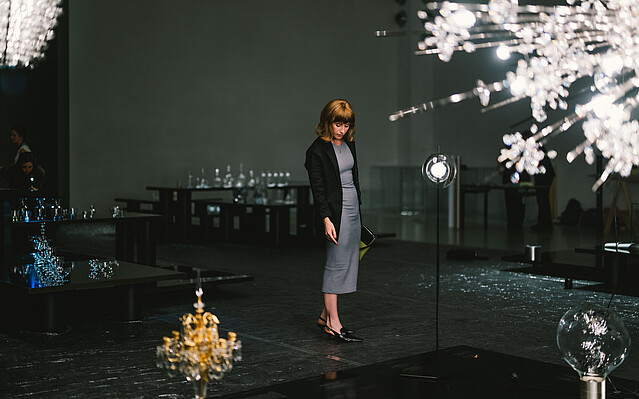 Lobmeyer_c_Wirtschaftsagentur_KarinHackl Lobmeyer: Eine Frau steht in einem dunklen Raum und um sie sind Kronleuchter aus Glas